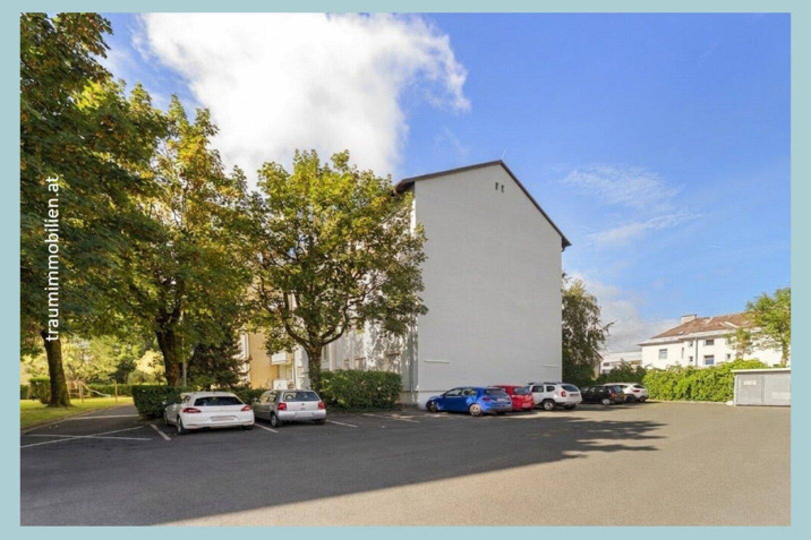 Außenparkplätze neben einem Wohngebäude umgeben von Bäumen.