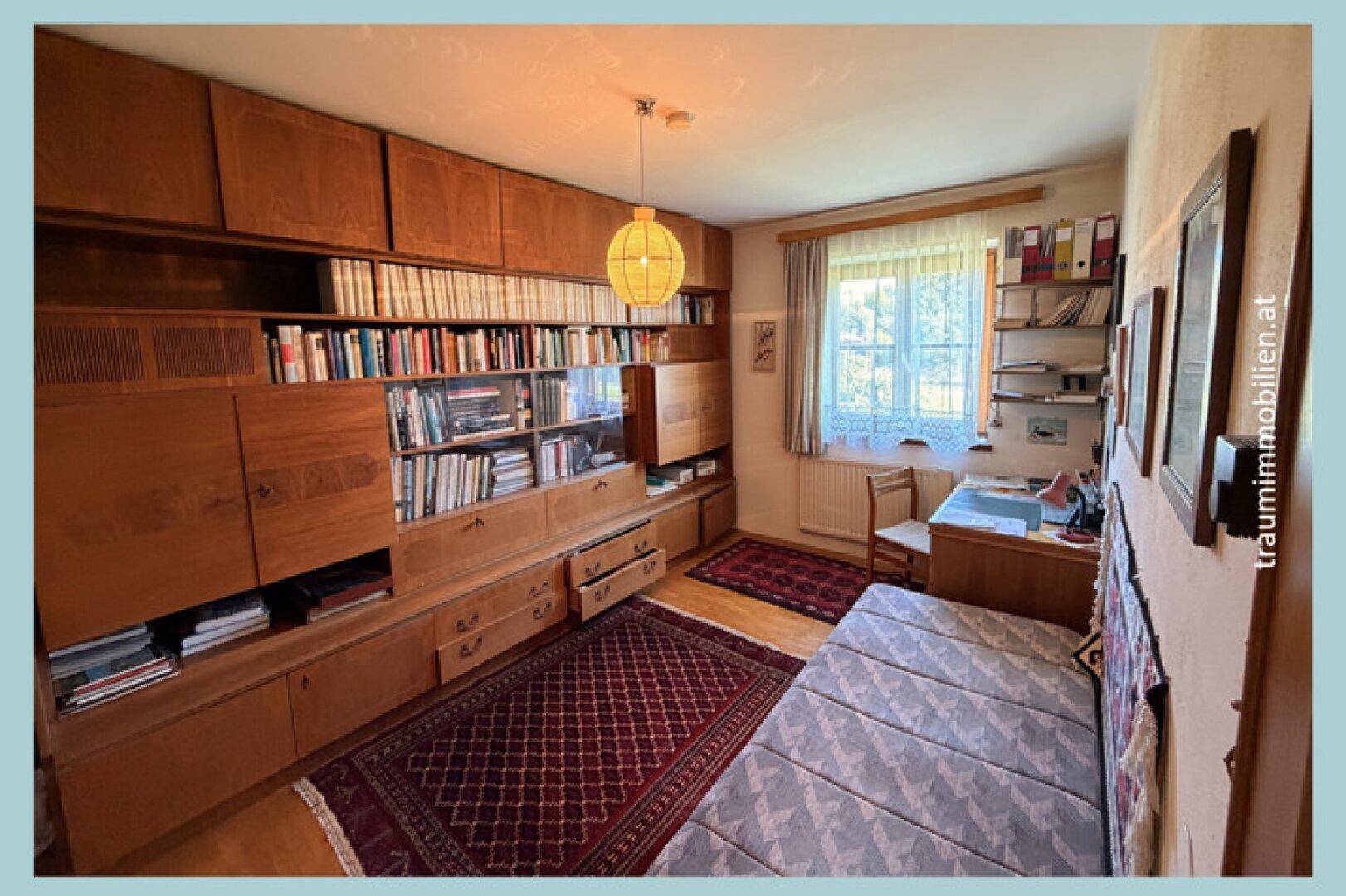 Arbeitszimmer mit großer Holzregalwand, Schreibtisch und Tageslicht.