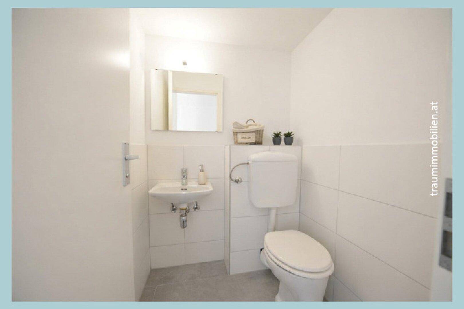 Helles Gäste-WC mit weißen Wandfliesen, grauem Boden und kleinem Waschbecken.