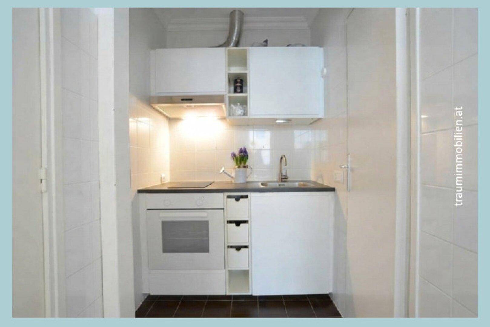 Kleine, funktionale Küchenzeile mit weißen Schränken, Kochfeld und Backofen, ideal für Pausen.