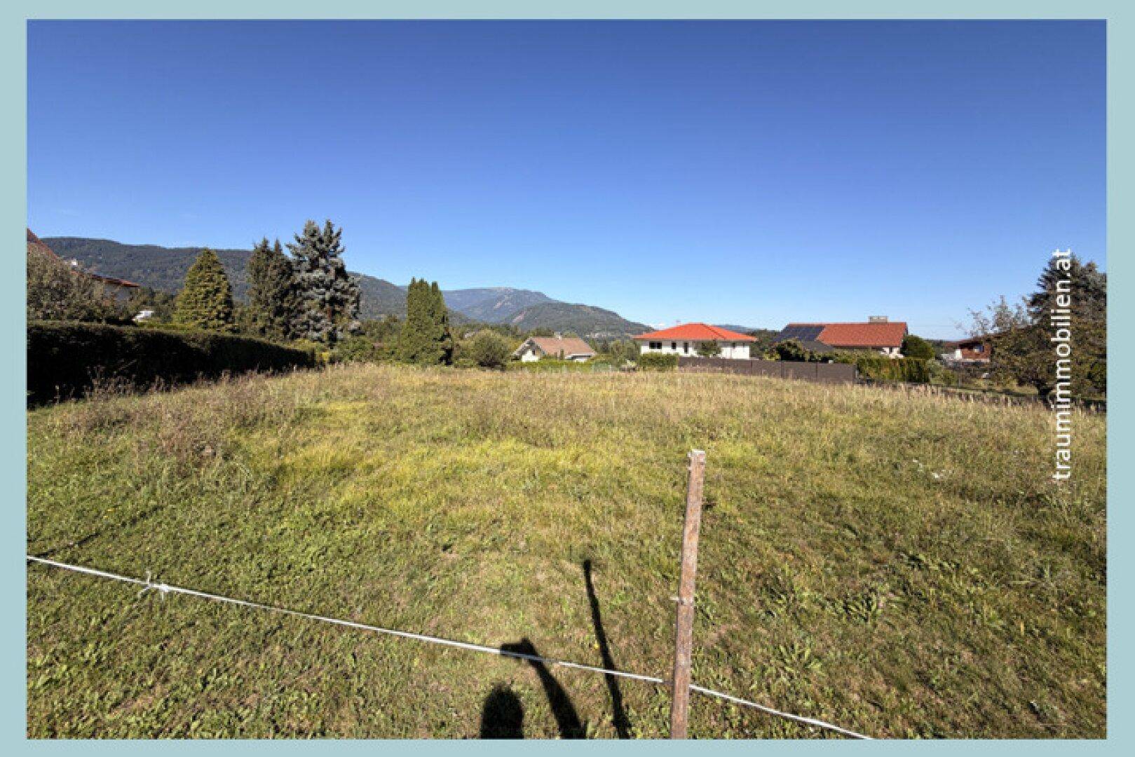 Weitläufiges, leicht hügeliges Wiesengrundstück mit Blick auf die umliegende Bebauung und die Berglandschaft.
