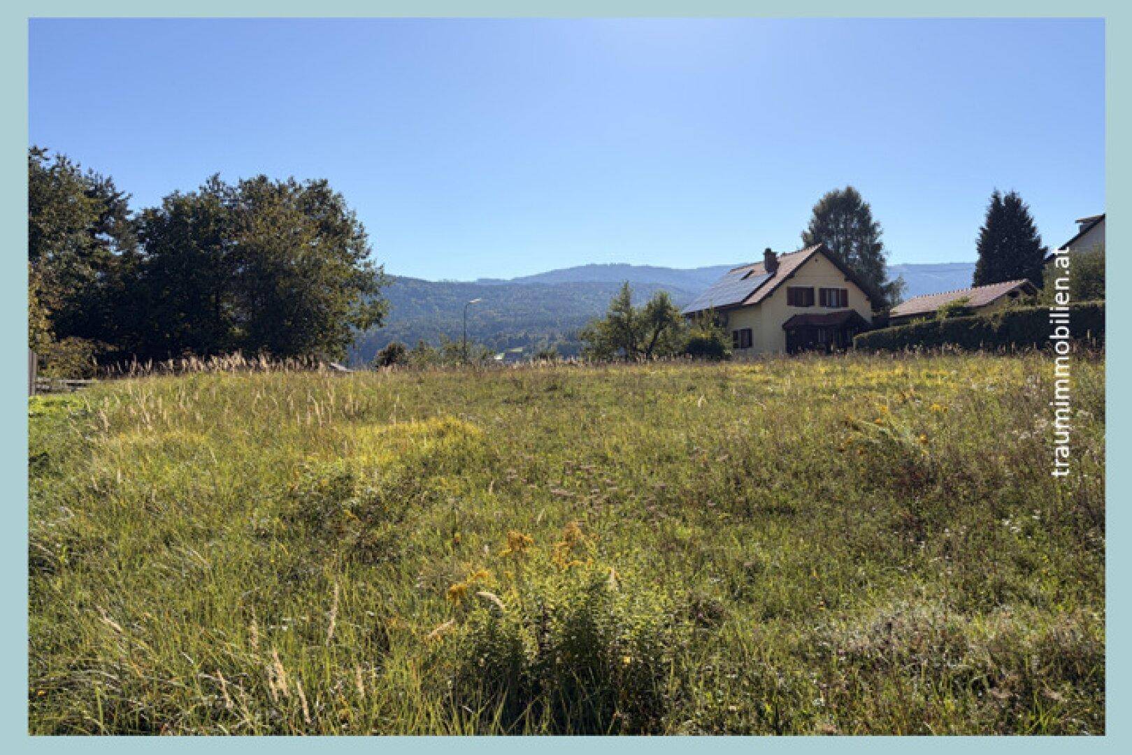 Weitläufiges Wiesengrundstück mit einem Haus im Hintergrund und einem Panoramablick auf die sanften Berge.