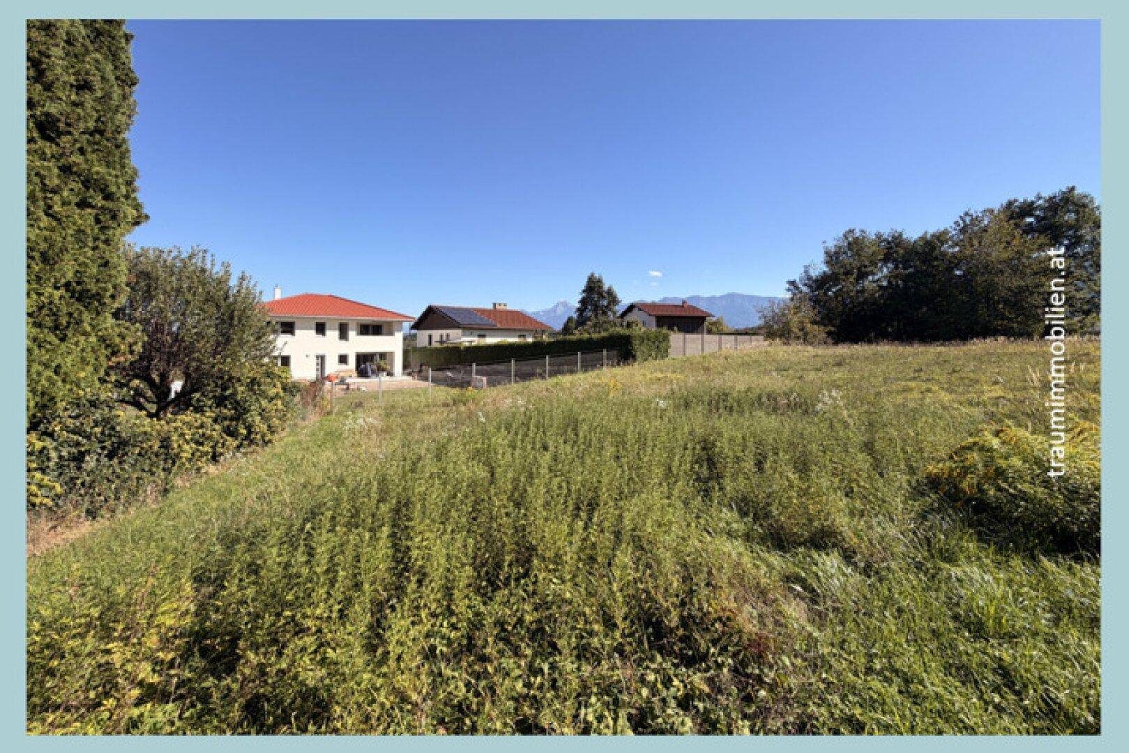Weitläufiges Wiesengrundstück mit angrenzenden Häusern und einem weiten Blick auf die umliegende Bergwelt.