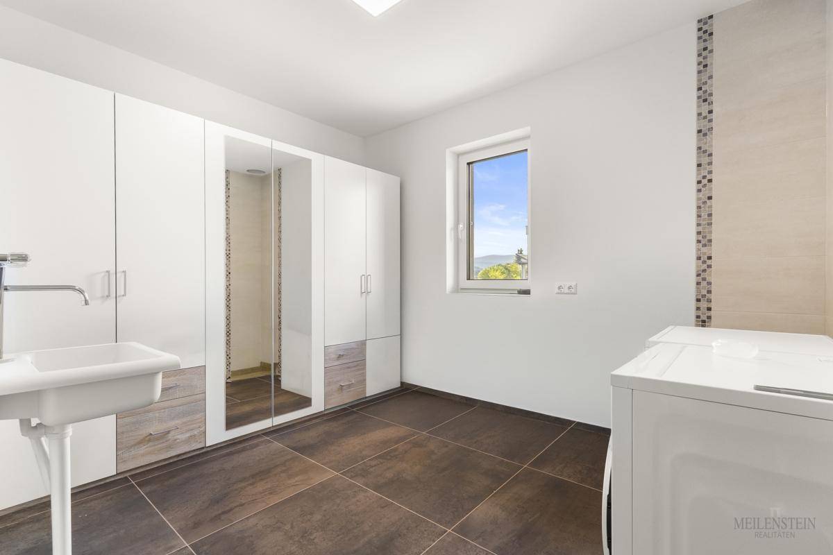 Praktischer Hauswirtschaftsraum mit Waschbecken, Schränken und Fenster mit Ausblick.