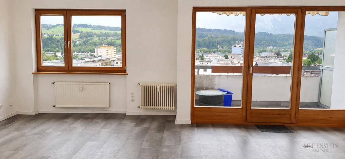 Geräumiger Wohnbereich mit hellem Laminatboden, großen Fenstern und direktem Zugang zum Außenbereich.