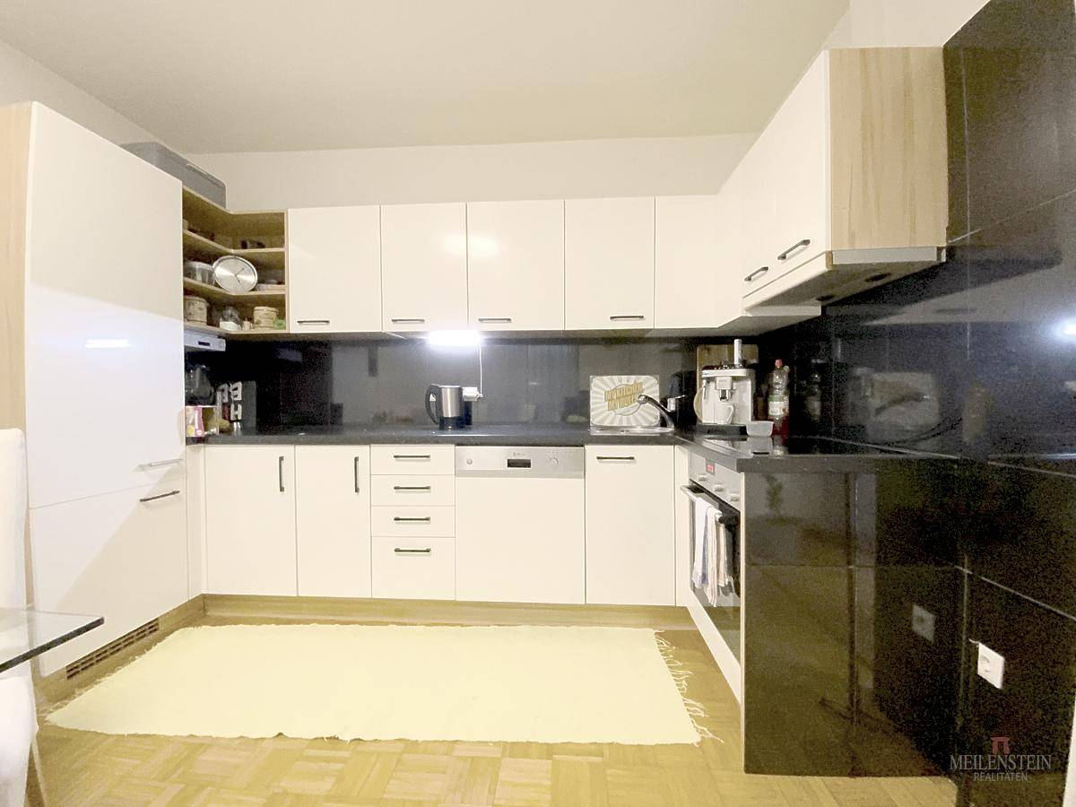 Moderne Küche mit weißen Hochglanzfronten, schwarzen Arbeitsplatten und integrierten Geräten.