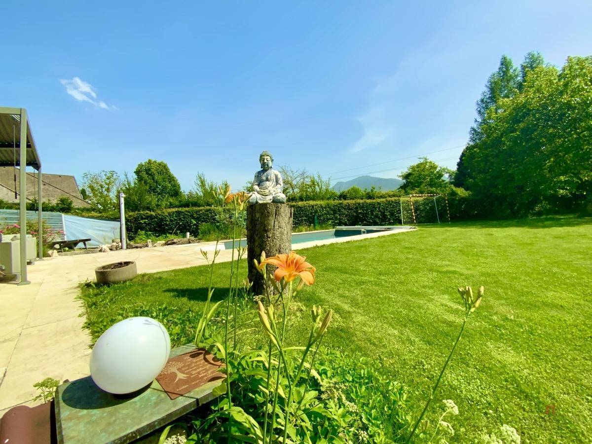 Sonniger Garten mit Rasen, Blumenbeeten und Blick auf die umliegende Natur.