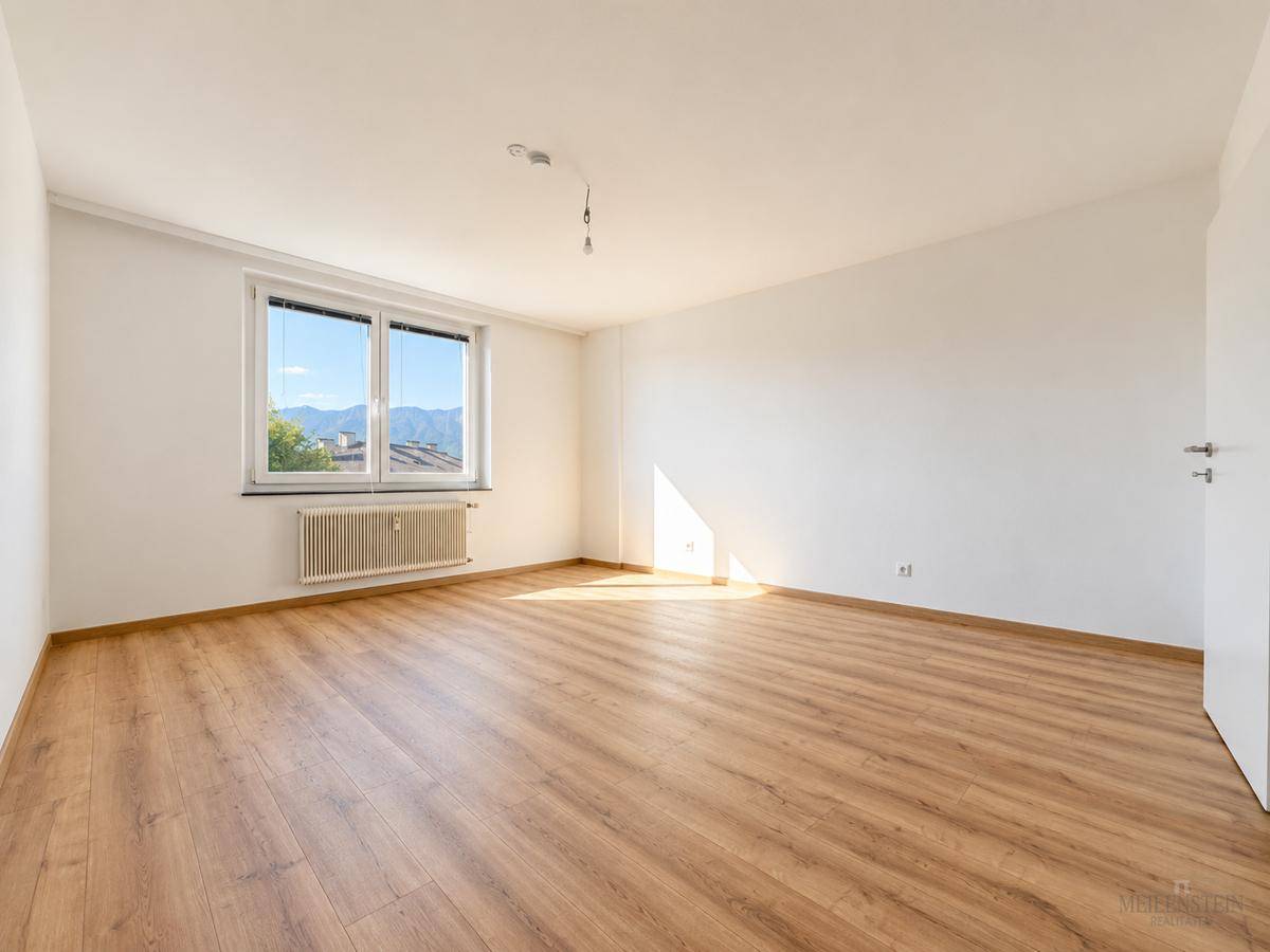 Geräumiger, heller Raum mit Laminatboden und einem großen Fenster, das viel Tageslicht hereinlässt.