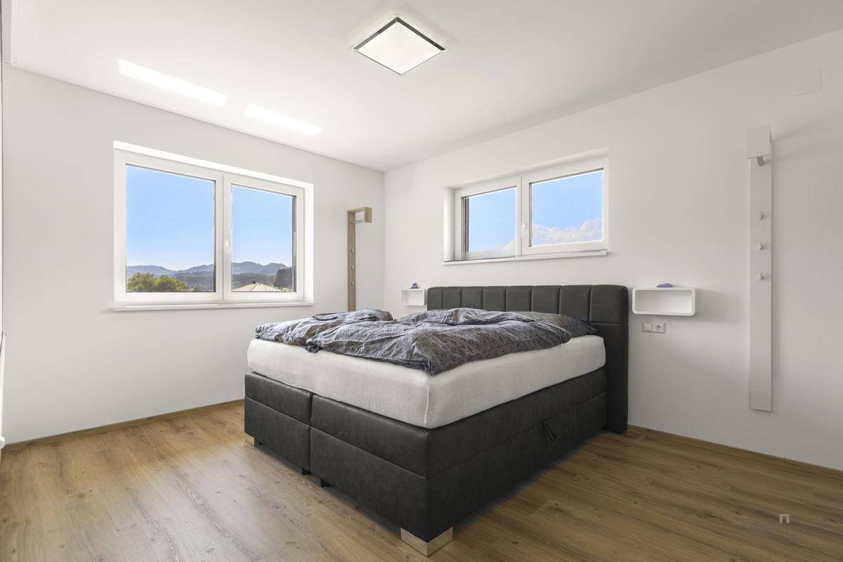 Helles Schlafzimmer mit Doppelbett, Holzboden und Fenstern mit Bergblick.