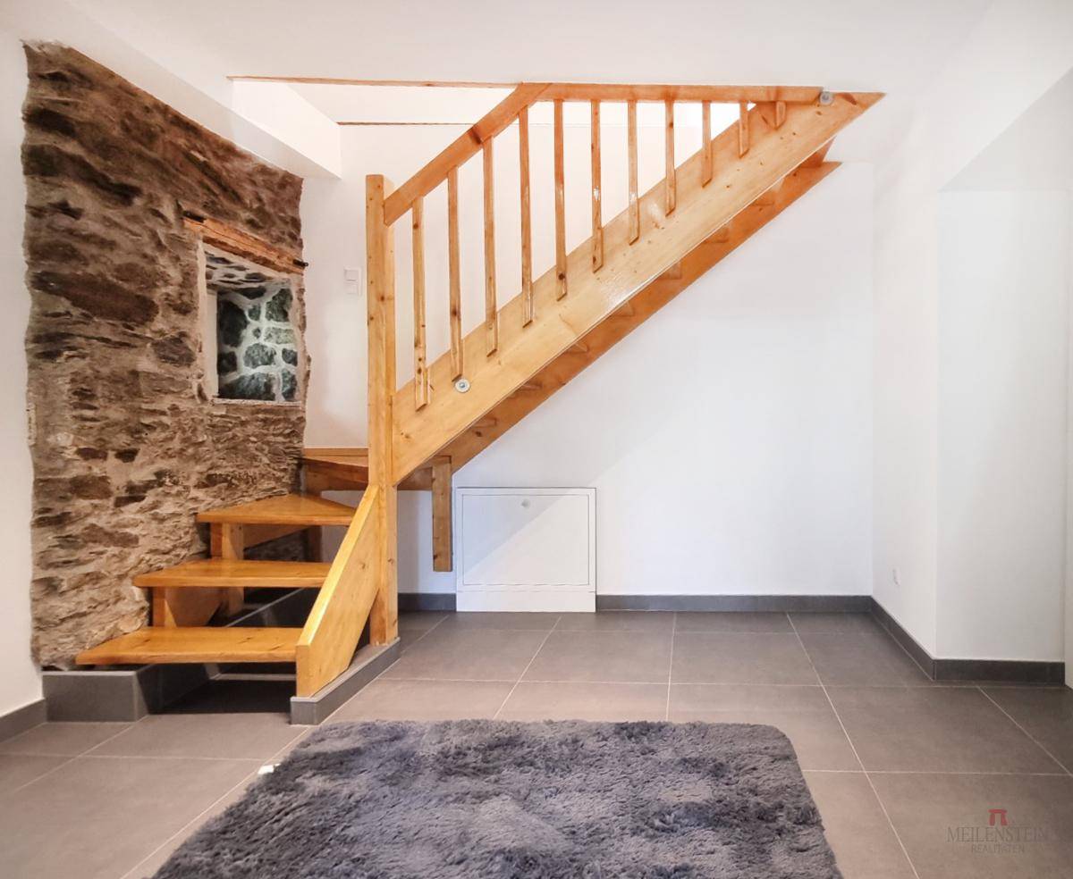 Eingangsbereich mit rustikaler Steinwand, Holztreppe und modernem Fliesenboden.