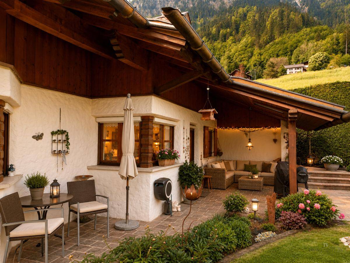 Überdachte Terrasse mit bequemen Lounge-Möbeln und Blick auf den Garten und die bewaldeten Berge.