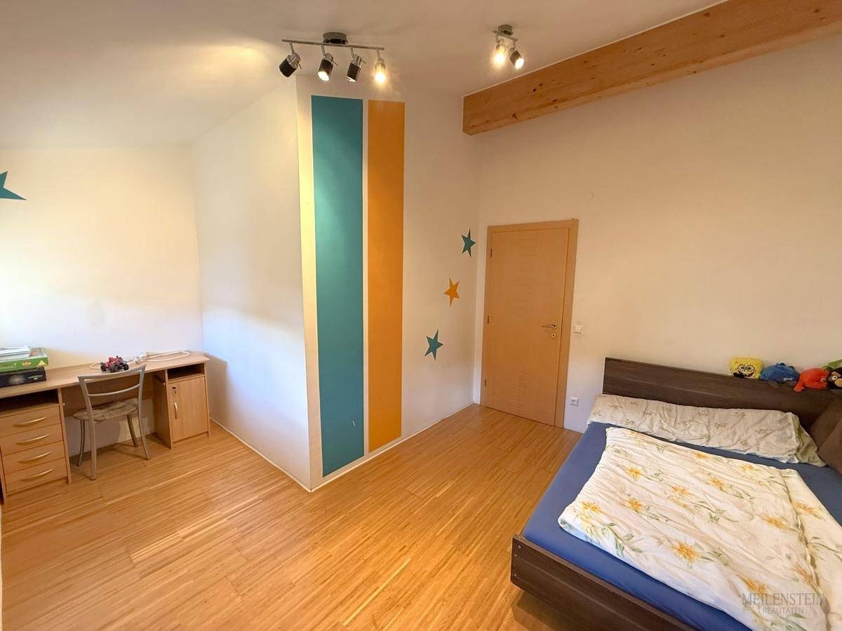Helles Kinderzimmer mit Holzboden, Schreibtisch und farbigen Akzenten an den Wänden.