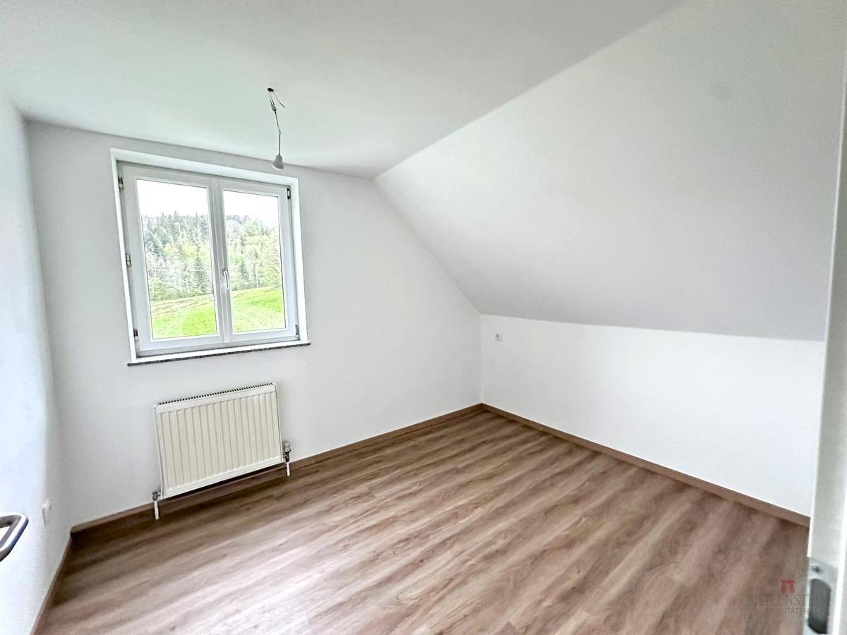 Schlafzimmer im Dachgeschoss mit schrägen Wänden, Laminatboden und Fenster mit Ausblick.
