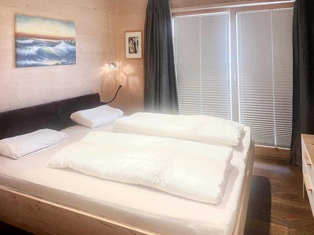 Gemütliches Schlafzimmer mit Holzwänden, Doppelbett und großen Fenstern für viel Licht.