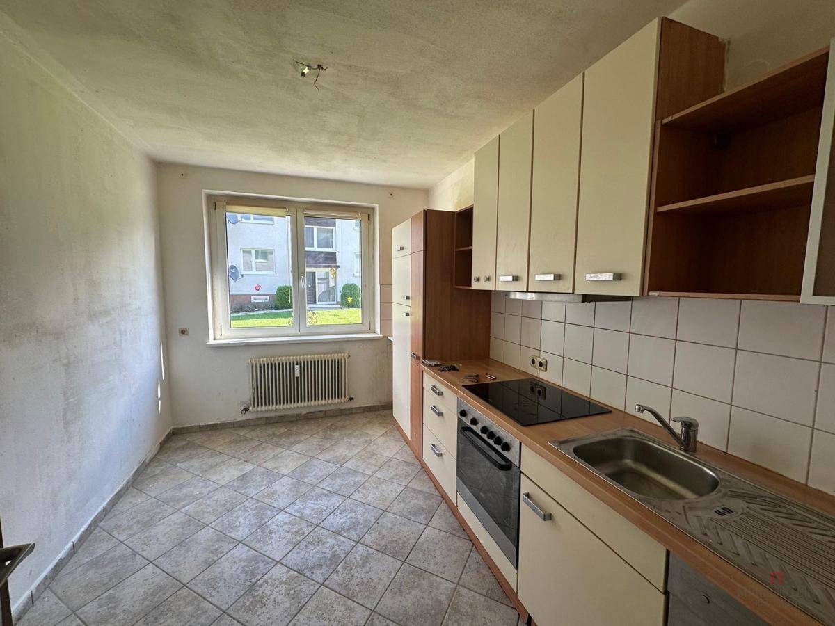 Ältere Küche mit Fenster, Heizkörper und Fliesenboden, die eine Modernisierung benötigt.