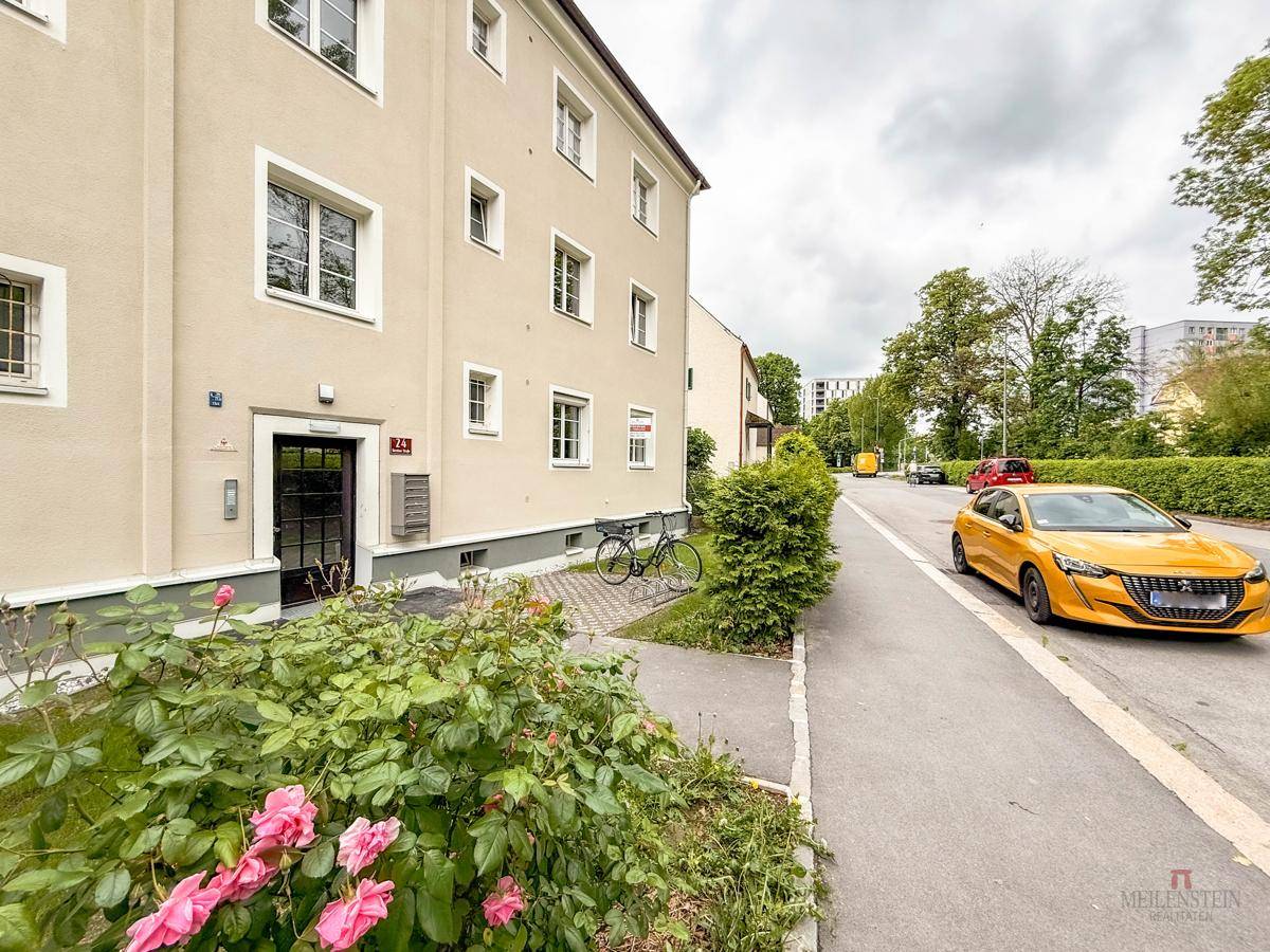 Straßenansicht eines Wohngebäudes mit Eingangsbereich und blühenden Rosen im Vorgarten.