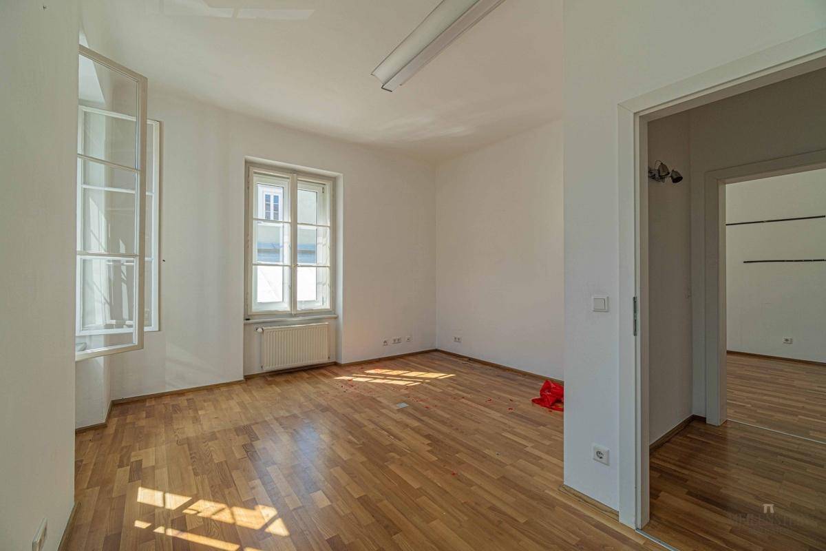 Heller Raum mit Holzboden und einem großen Fenster, das den Raum mit Tageslicht durchflutet.