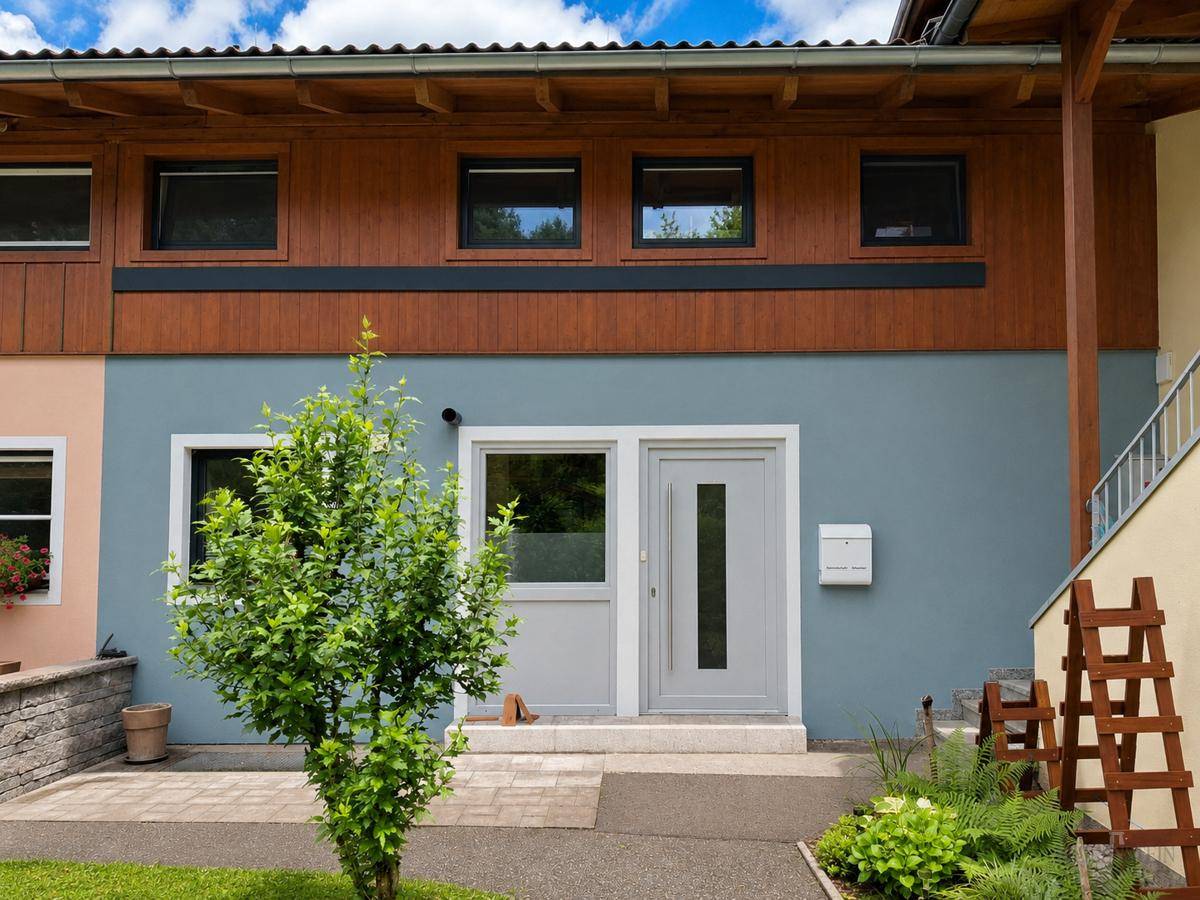 Moderne Hausfassade mit blauer und holzverkleideter Fläche sowie einer einladenden Eingangstür.