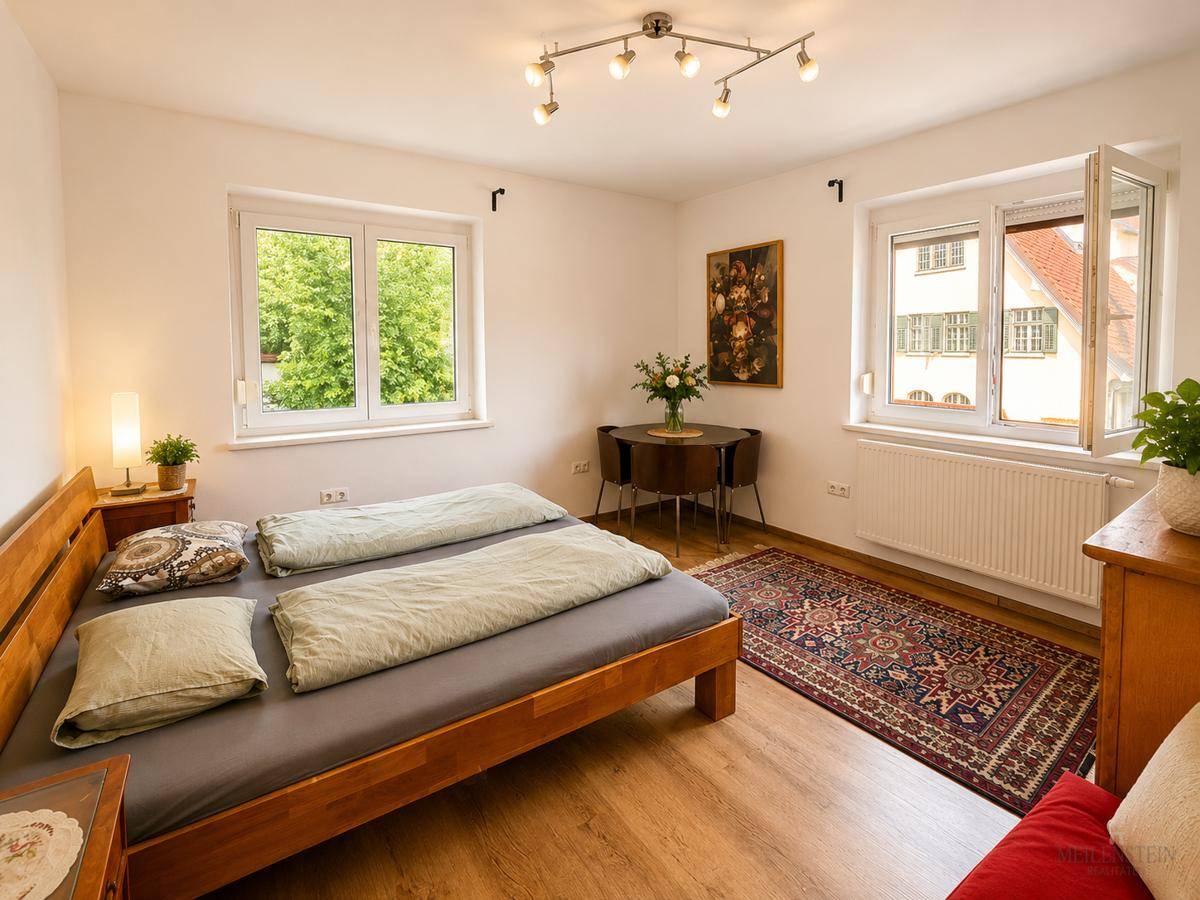 Helles Schlafzimmer mit Doppelbett, Teppich und zwei Fenstern für viel Tageslicht.
