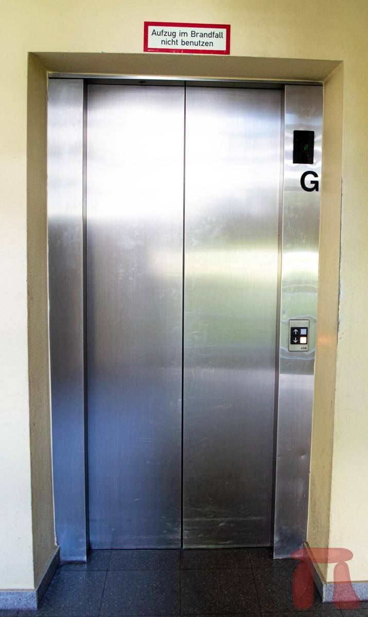 Aufzugstür aus Edelstahl im Flur eines Wohngebäudes mit Hinweisschild über Brandfallnutzung.