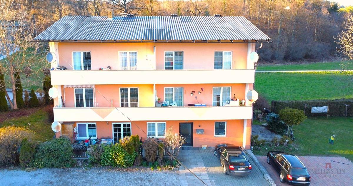 Vorderansicht des Wohngebäudes mit Eingangsbereich, Parkplätzen und grüner Umgebung.