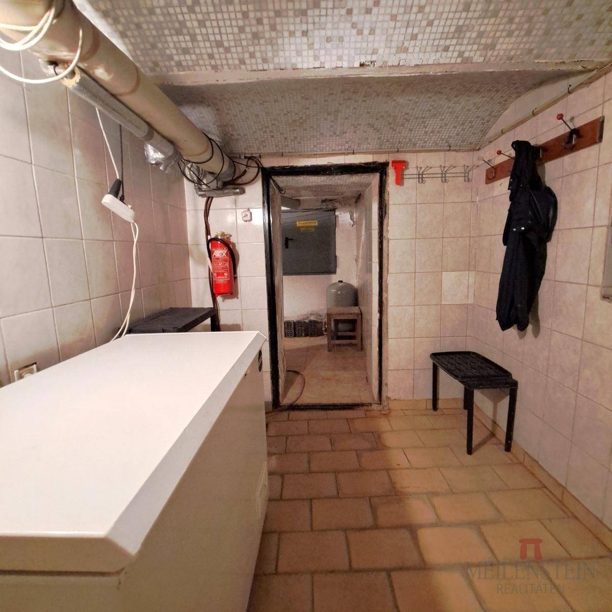 Kellerraum mit Fliesenboden, Gefriertruhe und Zugang zu weiteren Kellerräumen.