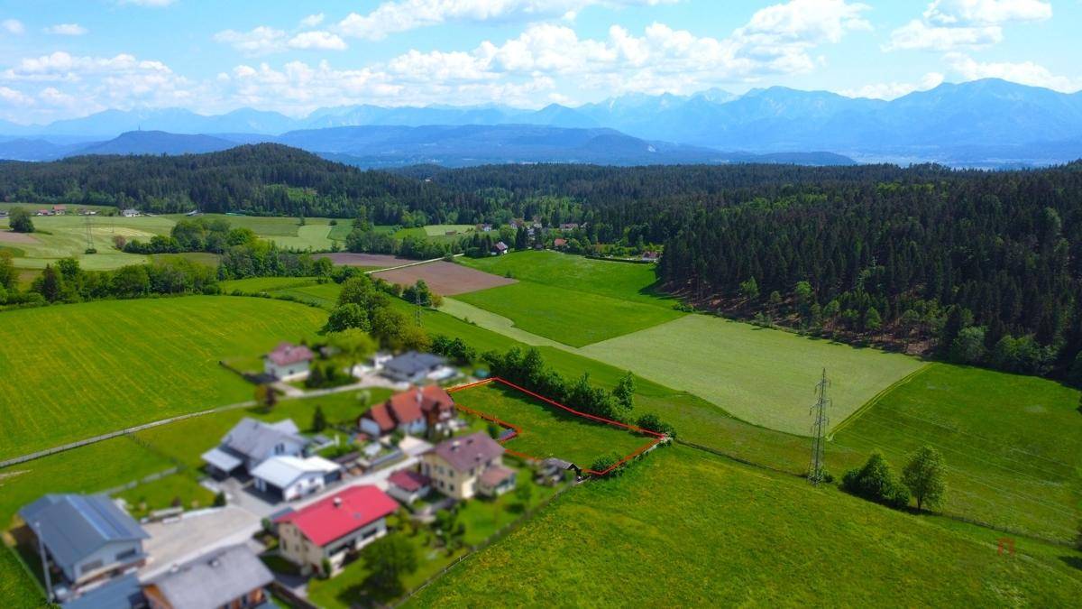 Weitläufige Luftaufnahme einer idyllischen Landschaft mit Häusern, Feldern und einer Bergkette am Horizont.