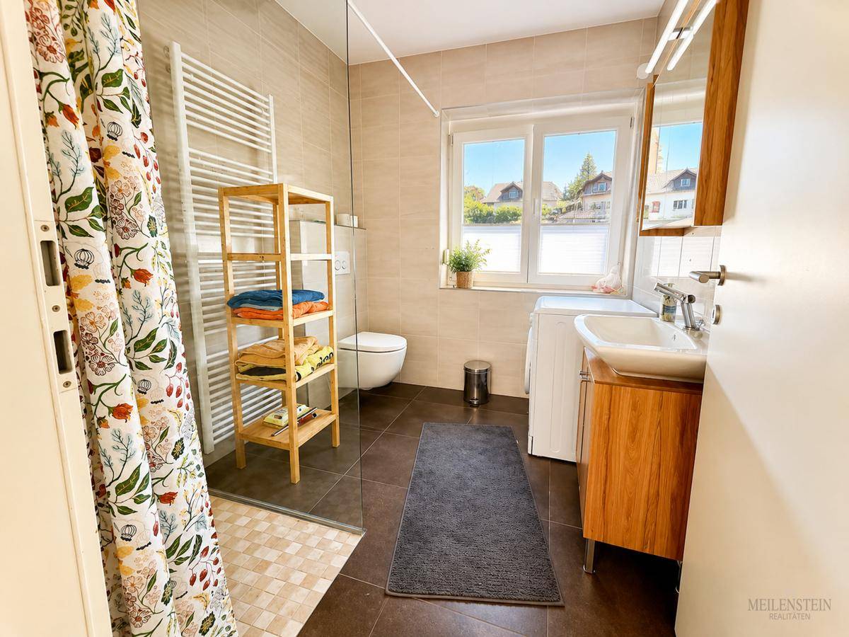 Modernes Badezimmer mit Dusche, Waschbecken, WC und Fenster für natürliches Tageslicht.