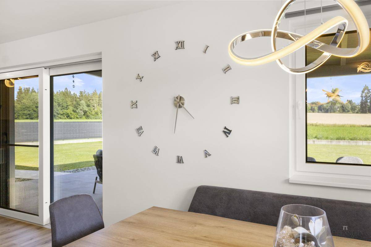Essbereich mit großem Wanduhr-Design, Holztisch und Zugang zur Terrasse mit Gartenblick.