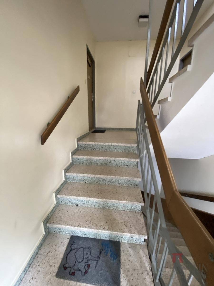 Heller Treppenaufgang mit Steinstufen und schlichtem Geländer in einem Mehrfamilienhaus.