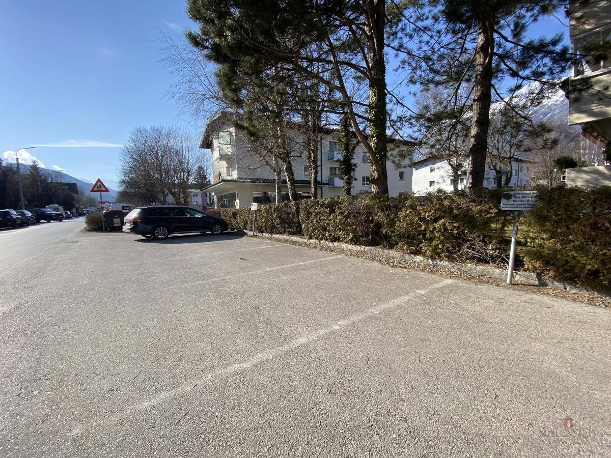 Außenparkplätze entlang einer Straße mit Hecken und Blick auf umliegende Gebäude.