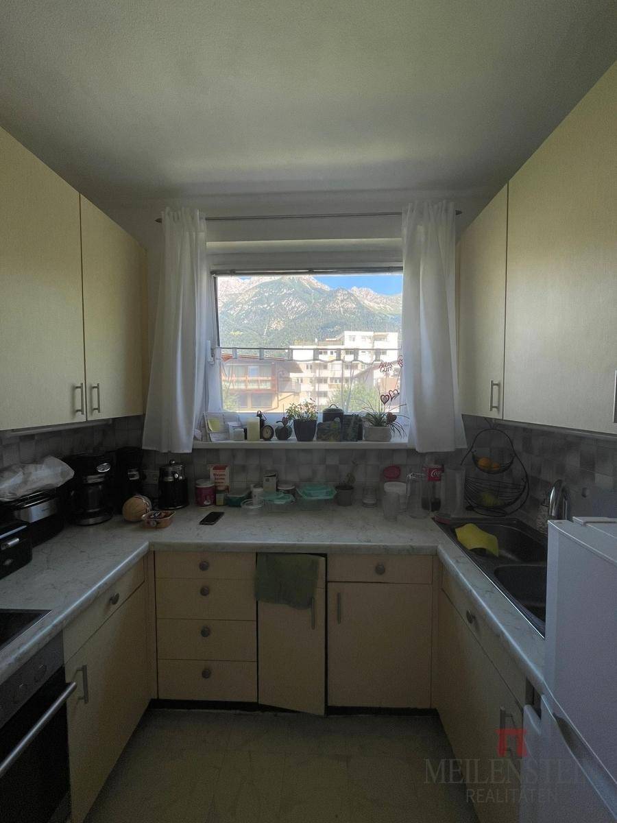 Küche mit U-förmiger Arbeitsplatte, hellen Schränken und Fenster mit Bergblick.