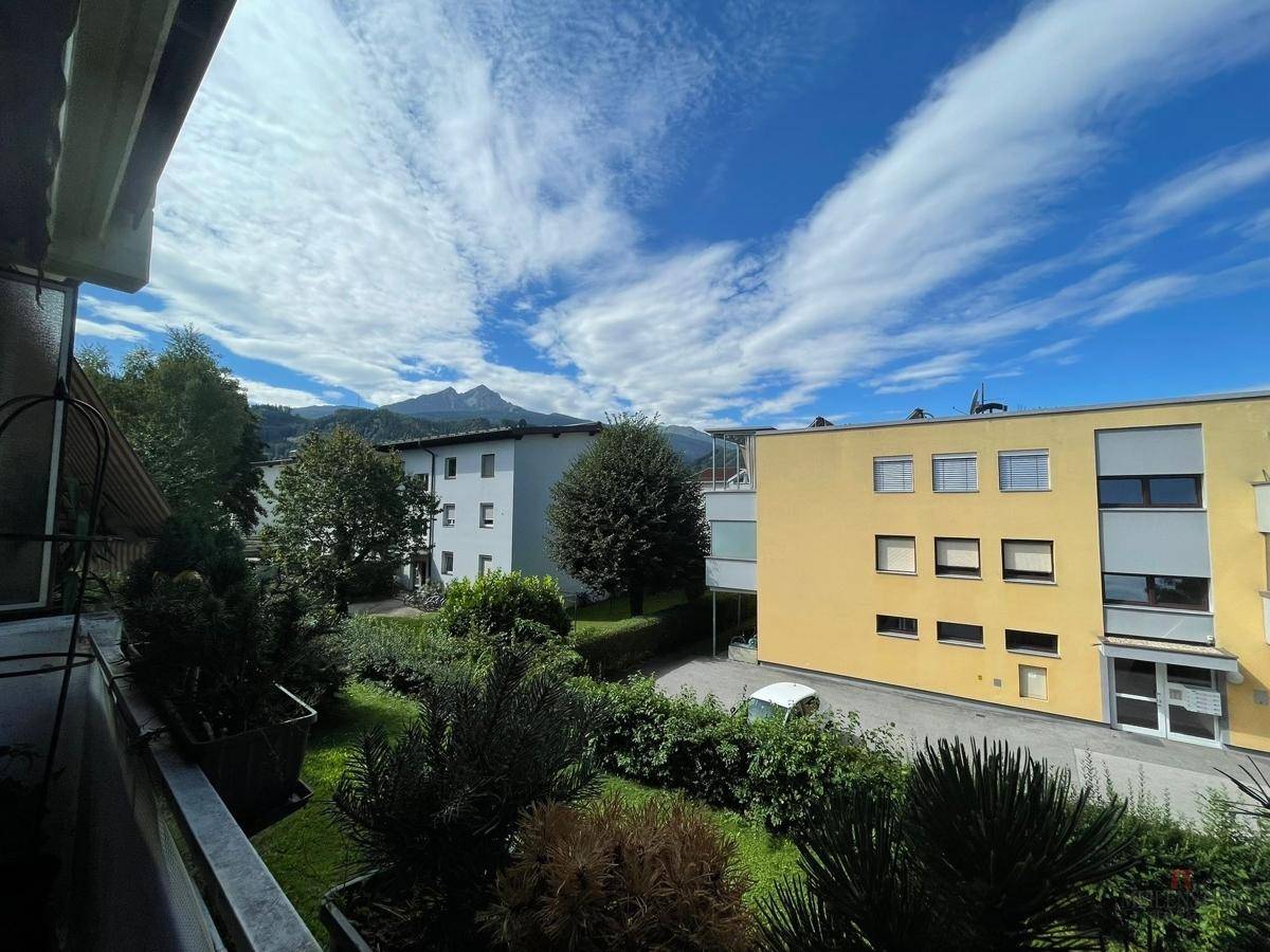 Balkon mit Blick auf die umliegenden Gebäude, Grünflächen und Berge.
