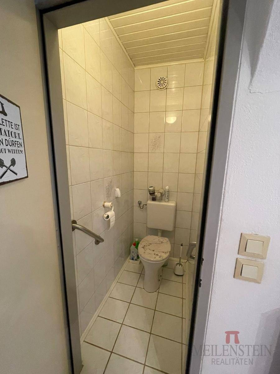 Separate Toilette mit Fliesen an Wänden und Boden, ausgestattet mit Haltegriff.
