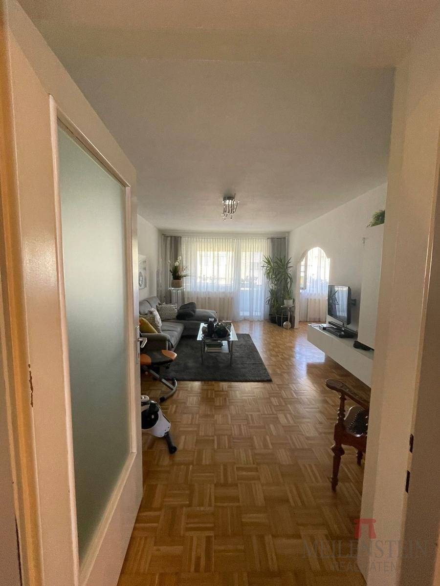 Geräumiges Wohnzimmer mit Parkettboden, Sofa und Fernseher, hell und einladend.