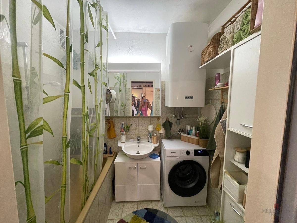 Kleines Badezimmer mit Dusche, Waschbecken und Waschmaschine, funktional eingerichtet.