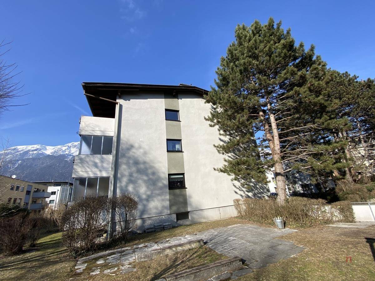 Rückseite des Wohnhauses mit hohen Bäumen und Bergblick unter blauem Himmel.