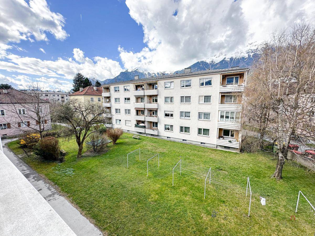 Außenansicht des Wohngebäudes mit Gemeinschaftsgarten und Wäscheleinen, umgeben von Bergen.