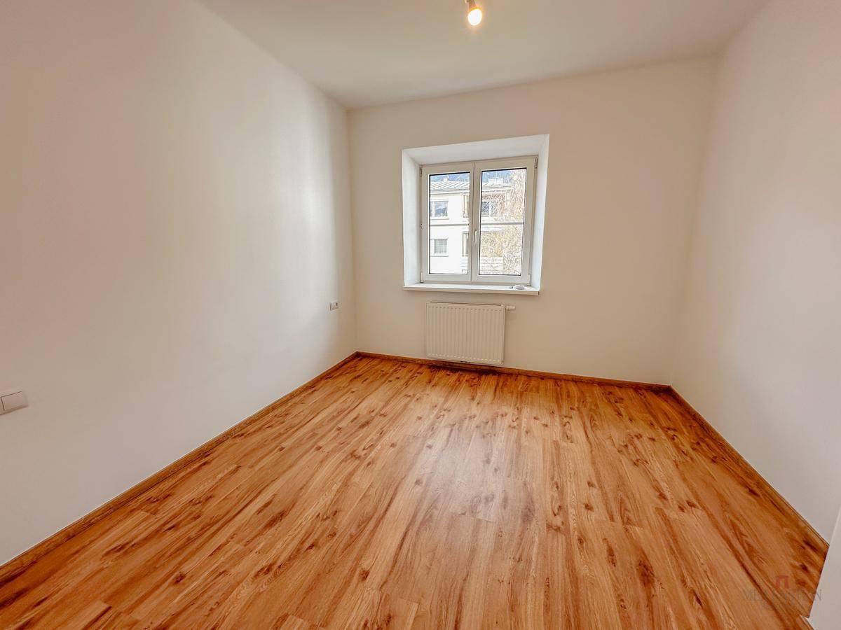 Helles Zimmer mit Holzboden und einem Fenster, bietet eine neutrale Basis für die Einrichtung.