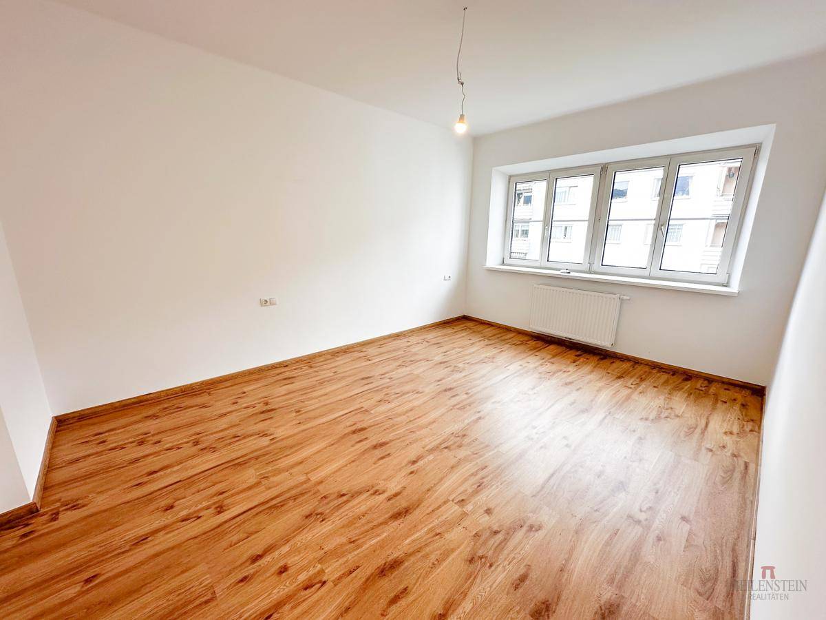 Lichtdurchfluteter Raum mit Holzboden und breitem Fenster, bietet vielseitige Nutzungsmöglichkeiten.