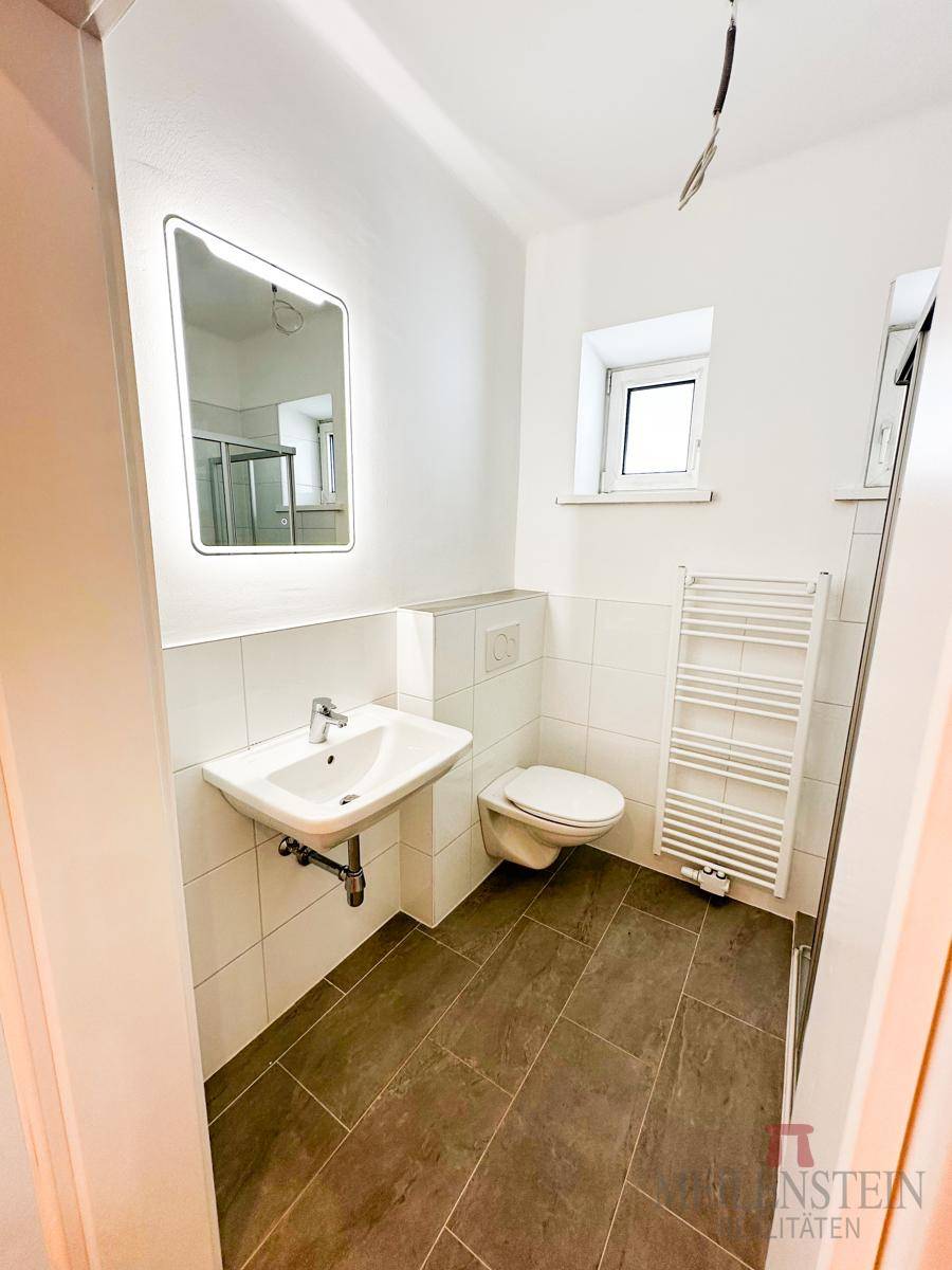 Modernes Badezimmer mit Dusche, Waschbecken, WC und beheiztem Handtuchhalter.