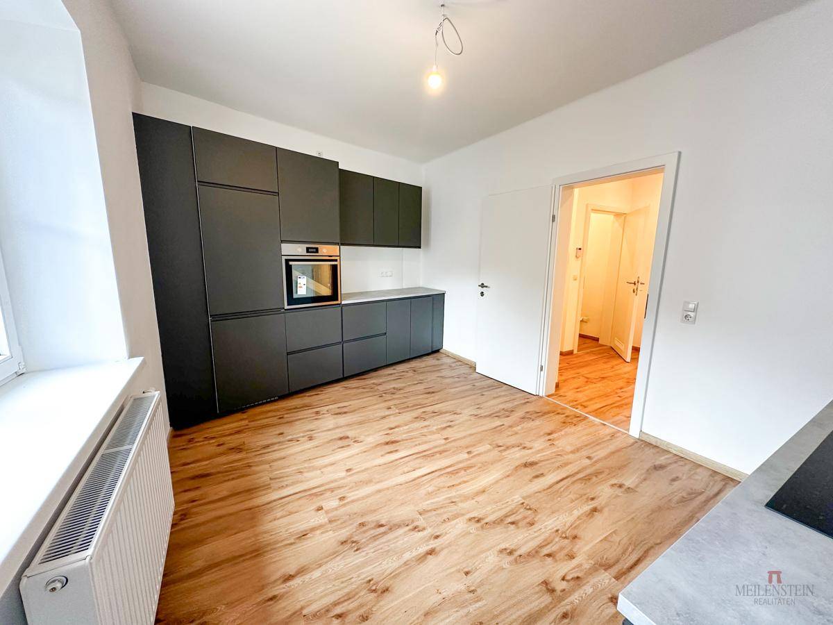 Moderne Einbauküche mit dunklen Schränken, Backofen und Holzboden, offen zum Flur.