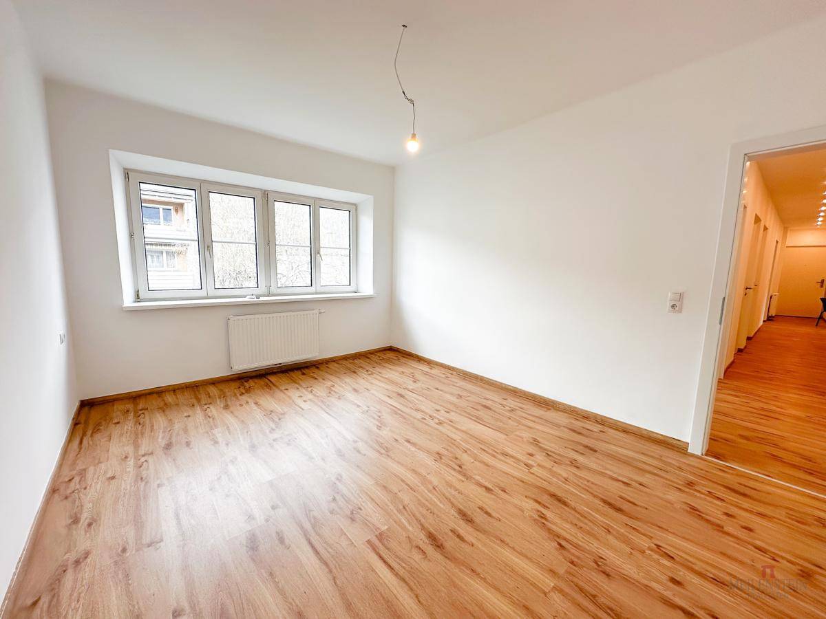 Helles, geräumiges Zimmer mit großem Fenster und Holzboden, ideal als Schlaf- oder Wohnzimmer.