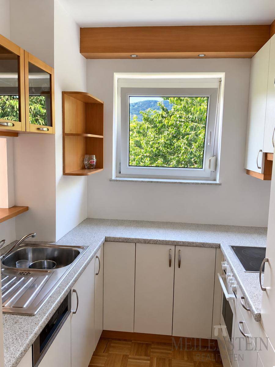 Kleine Küche mit weißen Schränken, Granit-Arbeitsplatte und Fenster mit Blick ins Grüne.