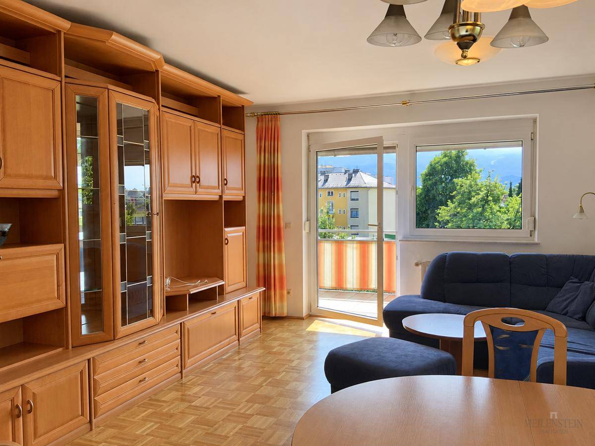Traditionell eingerichtetes Wohnzimmer mit Holzschrankwand, blauem Sofa und Zugang zum Balkon.