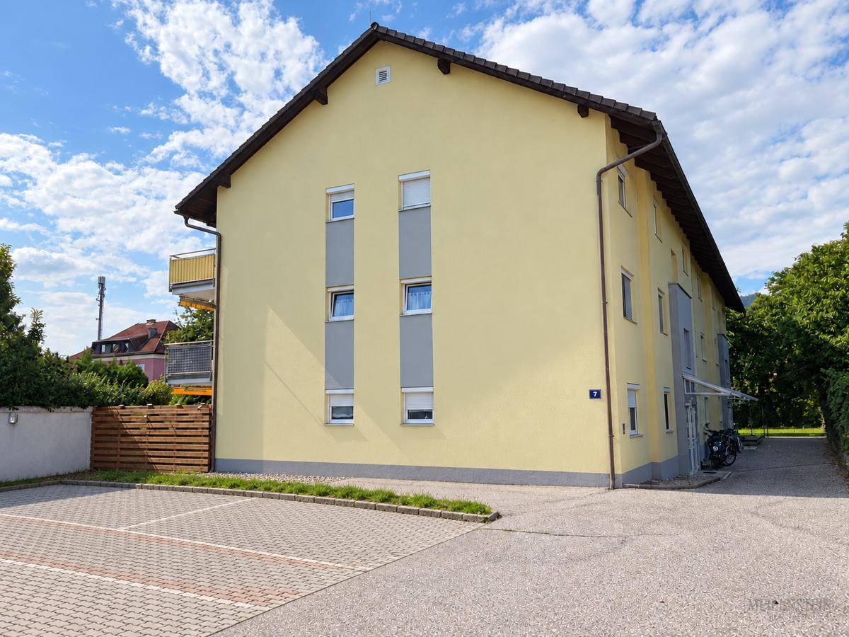 Außenansicht des Wohngebäudes mit gelber Fassade und leerem Parkplatzbereich.