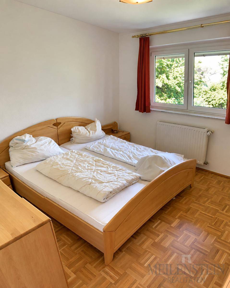 Schlafzimmer mit Holzdoppelbett, Nachttischen und Parkettboden, mit Blick ins Grüne.
