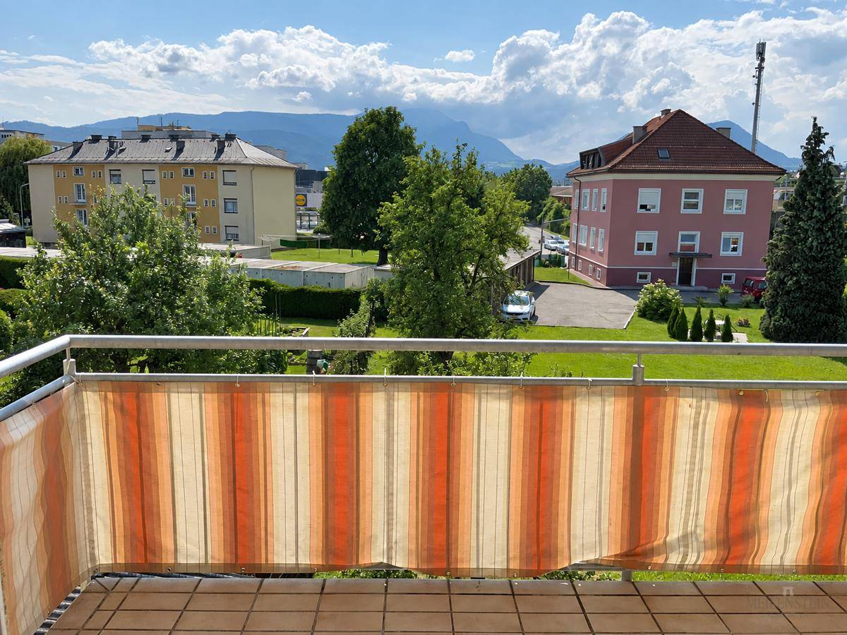 Weitblick vom Balkon über die Stadt, grüne Flächen und die umliegende Berglandschaft.