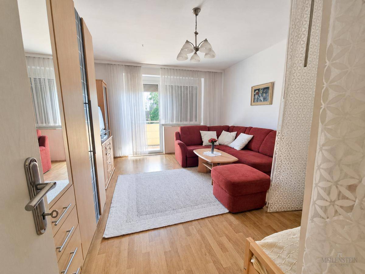 Geräumiges Wohnzimmer mit Holzboden, rotem Sofa und direktem Zugang zum Balkon.
