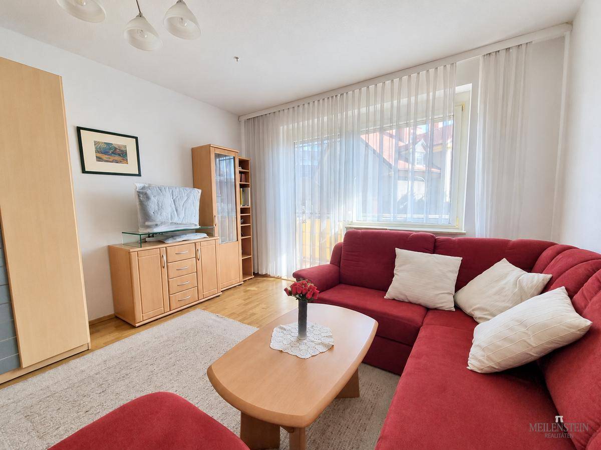 Gemütliches Wohnzimmer mit rotem Ecksofa, Holzmöbeln und viel Tageslicht.